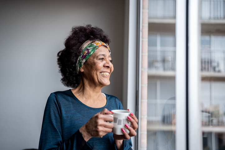 Smiling senior woman holding a coffee mug and looking out a window