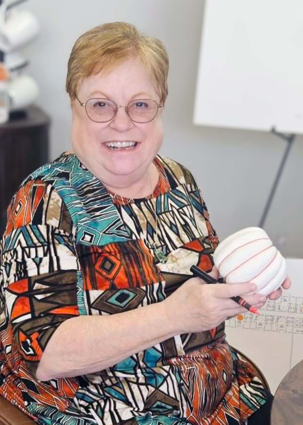 A senior woman smiles while working on an autumn themed pumpkin painting craft.