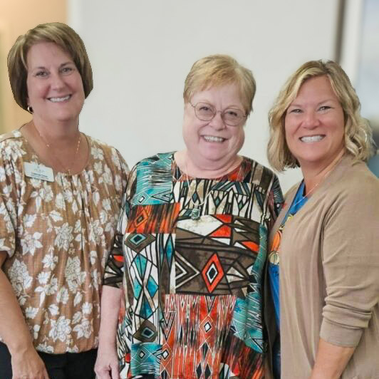 A senior woman smiles with two others during a joyful moment.