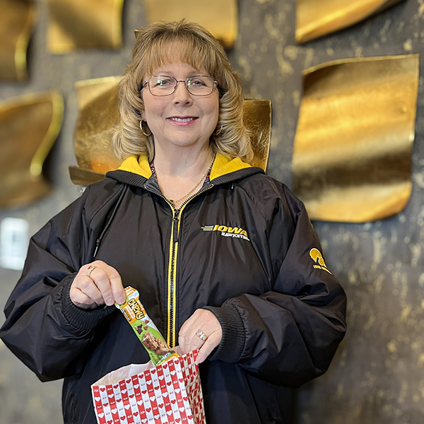 A woman on the Aura team smiles in front of an elegant gold-decorated wall at the community, displaying a gift bag.