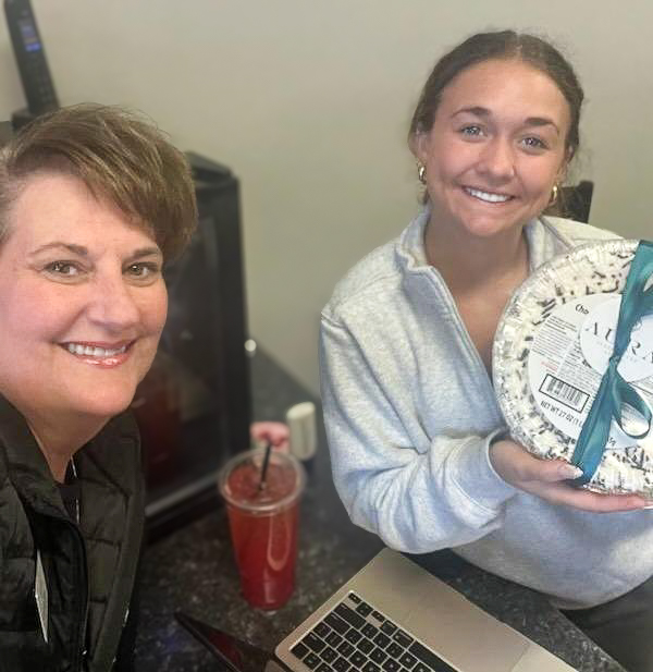 Two women smile, holding up a gift, at a local business.
